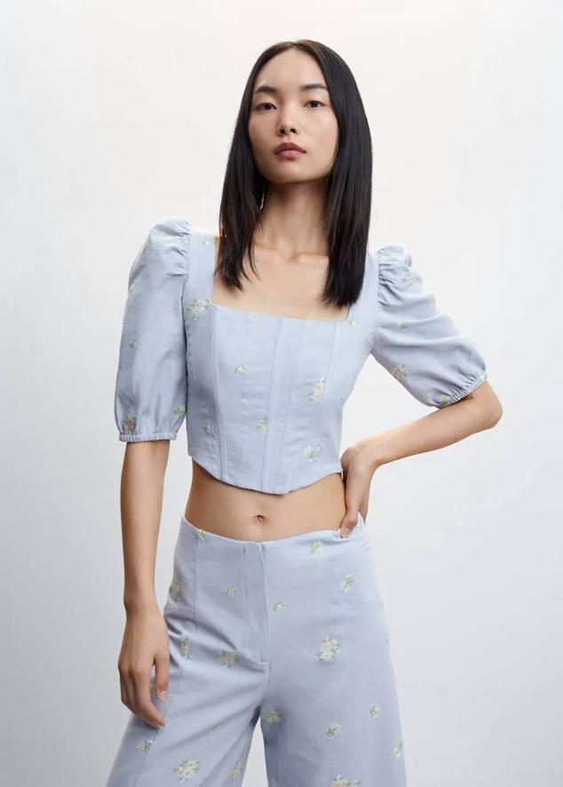 Blusa corsetera con escote cuadrado, elástico tipo nido de abeja en la espalda, mangas cortas abullonadas y bordados, en celeste, de Mango. La comprarás por 29,99 euros.