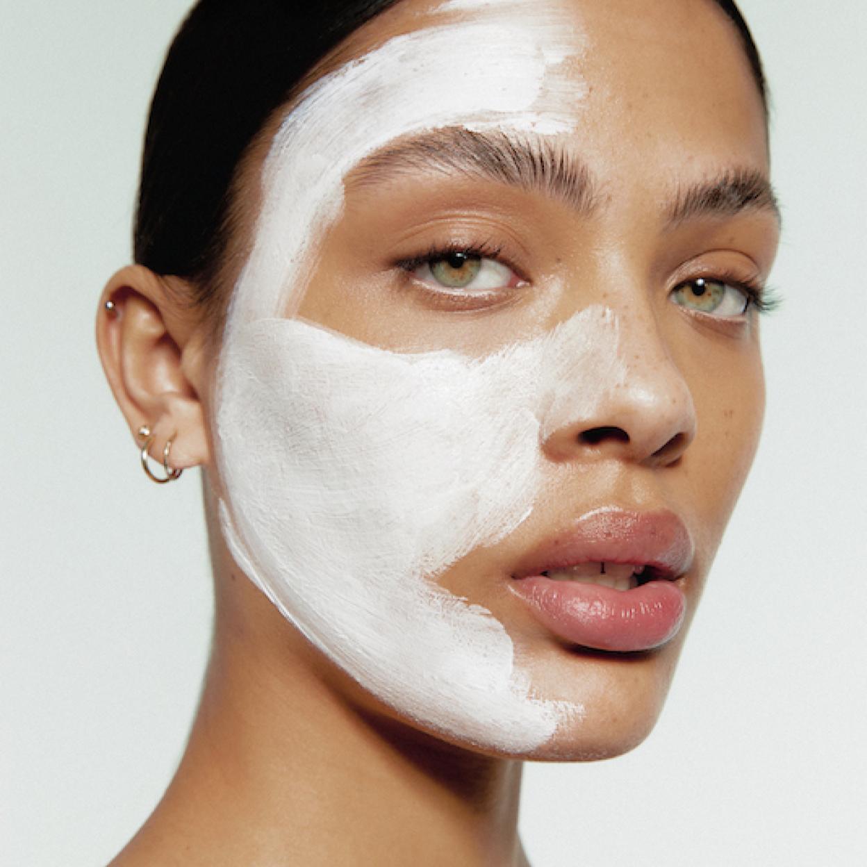 Una modelo se aplica una mascarilla exfoliante para piel grasa sobre el rostro.
