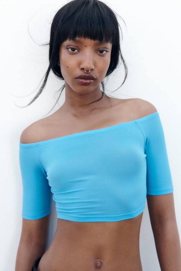  Camiseta crop entallada con escote recto, hombros al descubierto y manga corta, tono turquesa, de Zara. Consíguela a 9,95 euros.