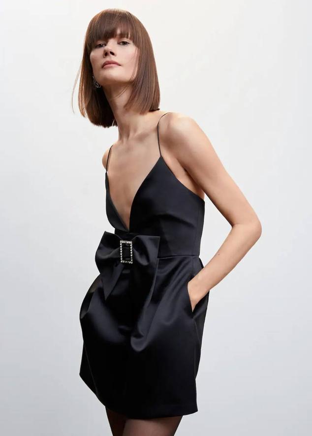 Vestido corto satinado con escote de pico, tirantes finos y detalle de maxi lazo con hebilla de strass, en negro, de Mango. Puedes encontrarlo a 69,99 euros.
