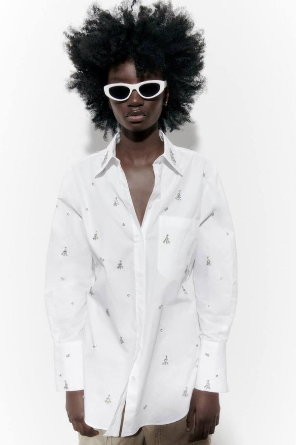Camisa de algodón oversize con cuello solapa, manga larga, bolsillo, cierre de botone y detalles bordados de joyas, en blanco. Cómprala a 49,95 euros.