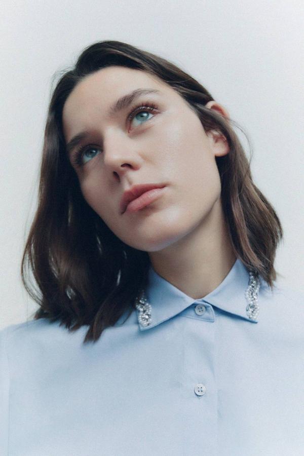 Camisa de popelín cropped con manga corta, cuello solapa decorado con joyas, cierre de botones y corte relajado, en celeste. Su precio es de 29,95 euros.