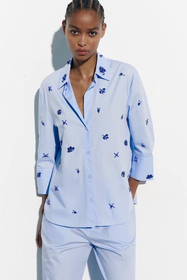 Camisa de popelín con cuello solapa, manga larga, cierre de botones y detalles de joyas azul, en celeste. Consíguela a 49,95 euros.