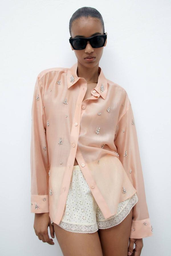 Camisa en tejido semitransparente con cuello solapa, manga larga, cierre de botones y decoración de joyas, en rosa. Está disponible por 49,95 euros.
