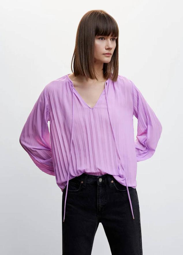 Blusa plisada con corte relajado, escote de pico, lazada y manga larga, tono lila, de Mango. Cuesta 19,99 euros.