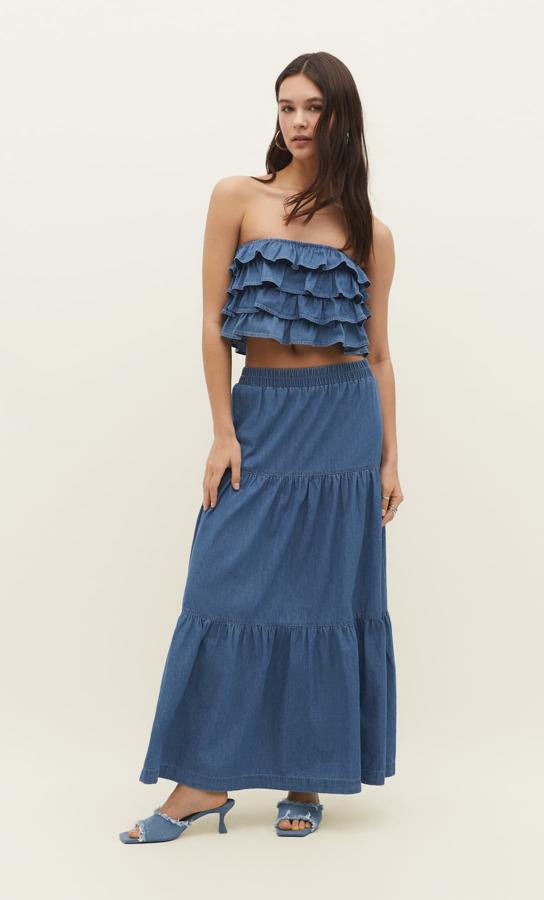 ¿Quién dijo que el denim es solo para prendas más gruesas? También las hay fluidas y est elook con falda larga (22,99 euros) y un top de volantes es lo más.
