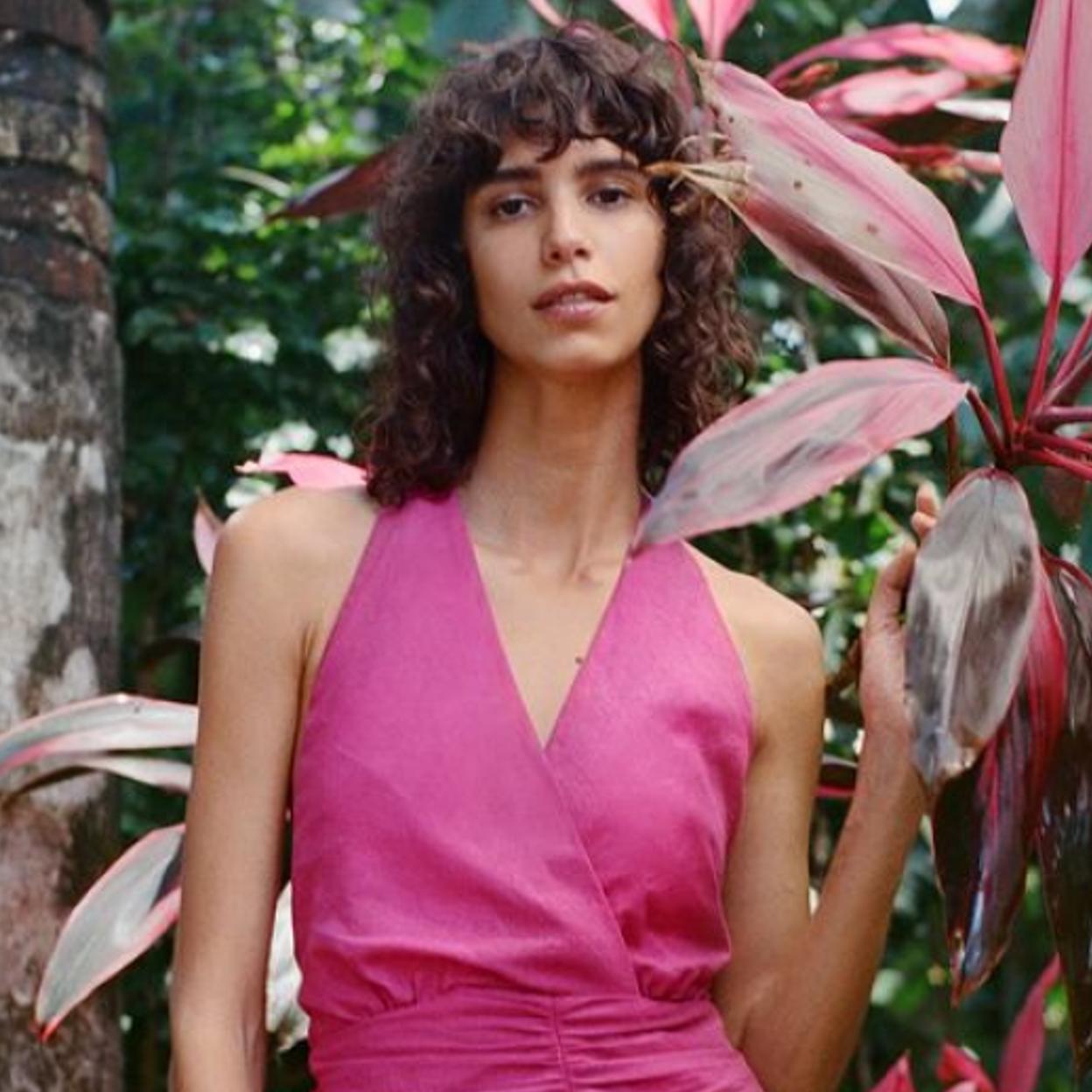 Una mujer con vestido fucsia rodeada de plantas.