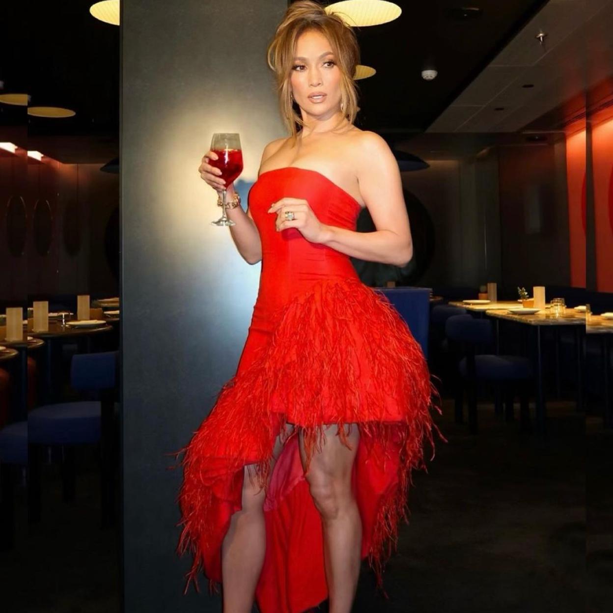 Jennifer Lopez con un vestido rojo de falda asimétrica mostrando sus tonificadas piernas. 