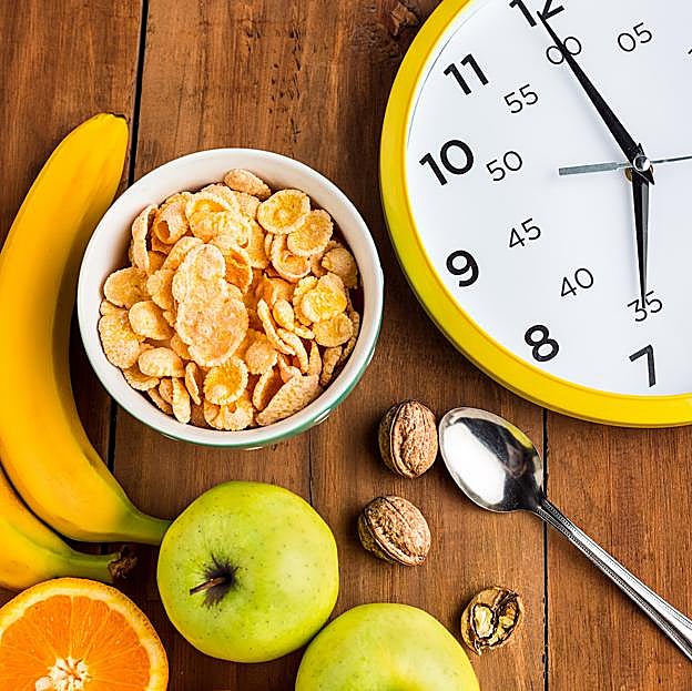 Reloj frente a un desayuno saludable con muesli, manzanas, frutas frescas y nueces.