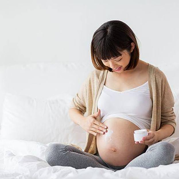 Mujer embarazada aplicando crema en la barriga
