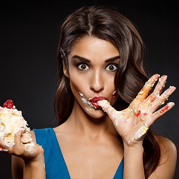Mujer chupándose los dedos mientras come un trozo de pastel. 