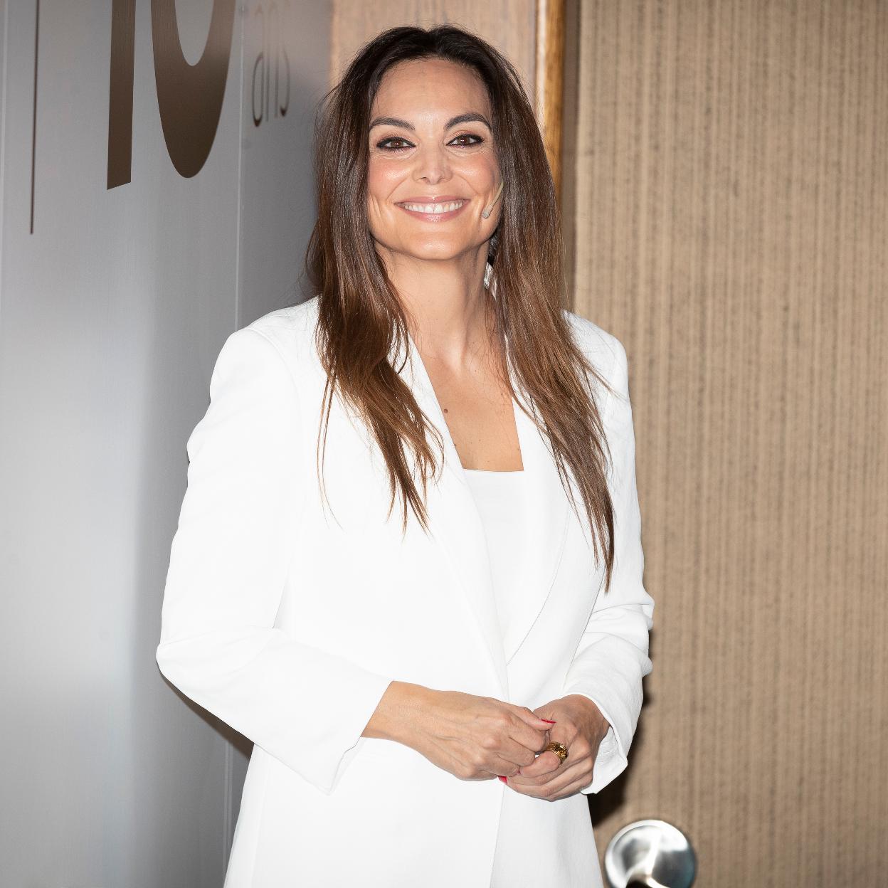 Mónica Carrillo posando para la cámara con un traje blanco. 