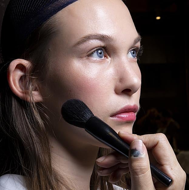 Un maquillador profesional aplicando el colorete a una modelo con una brocha ligera.