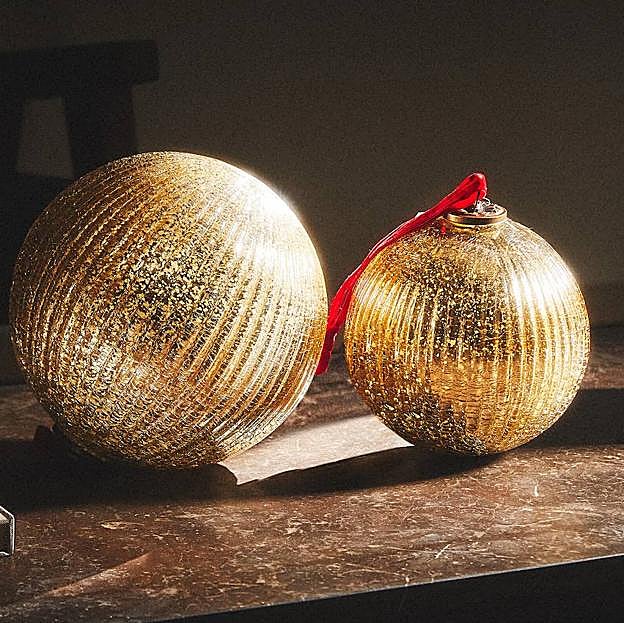 Imagen principal - Las bolas doradas y la guirnalda de flores cuestan 25.99 euros cada una. El adorno de Rey Mago de fieltro, 4.99 euros.