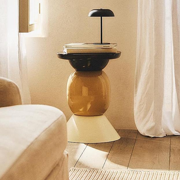 Imagen principal - La original mesa auxiliar es de la colección de Zara Home x La Collagerie y cuesta 99.90 euros. La butaca de madera y rafia es el modelo Java de Kenay (329 euros) y la estantería Daman es de Sklum y cuesta 169.95 euros.