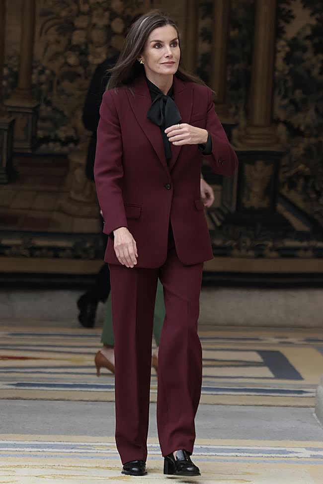 La reina Letizia con un traje burdeos y blusa con lazada.