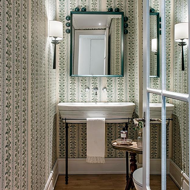 Baño de cortesía con paredes empapeladas y espejo a medida.