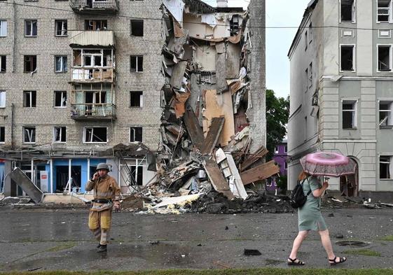 Una mujer pasa junto a un rescatista ucraniano que trabaja frente a un edificio parcialmente destruido tras un ataque con misiles rusos en Járkov.