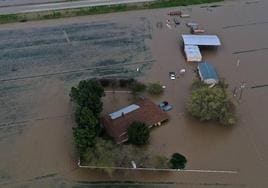 Una imagen aérea muestra una casa, vehículos y tierras de cultivo inundados durante una tormenta en el condado de Tulare, en California.