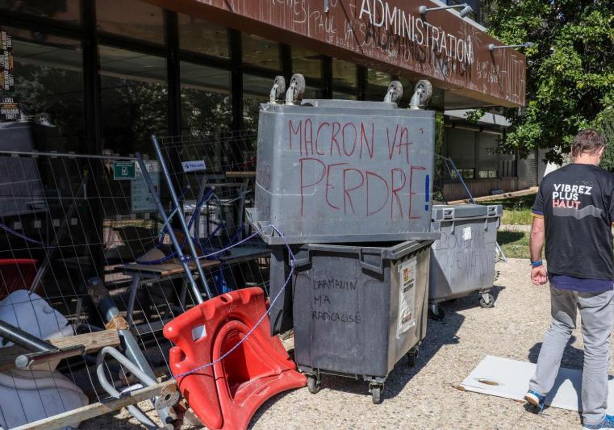 Un hombre camina frente a contenedores de basura en Montpellier en los que se observan eslóganes contra la reforma de pensiones de Macron.