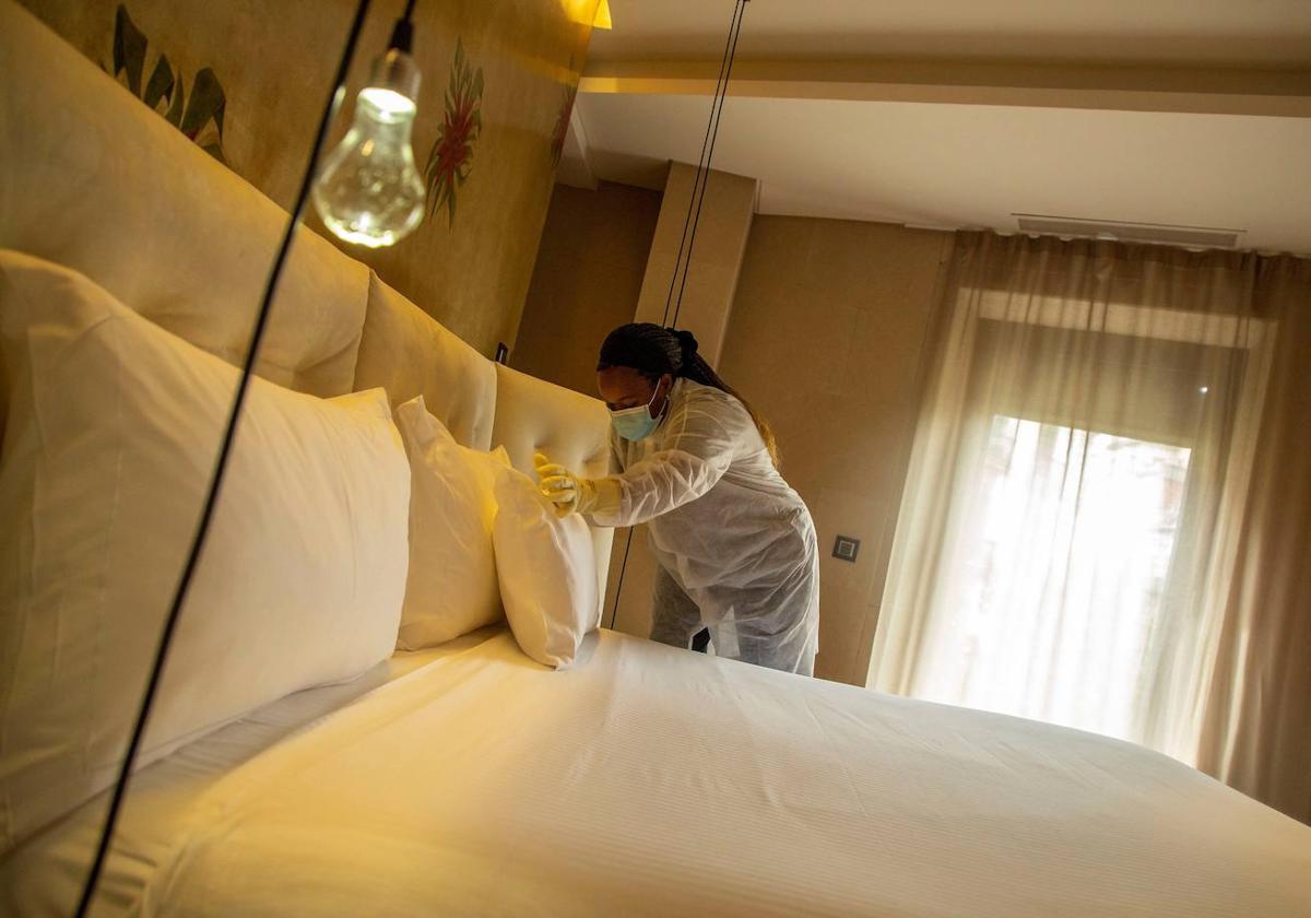 Una empleada arregla la cama en una habitación de hotel.