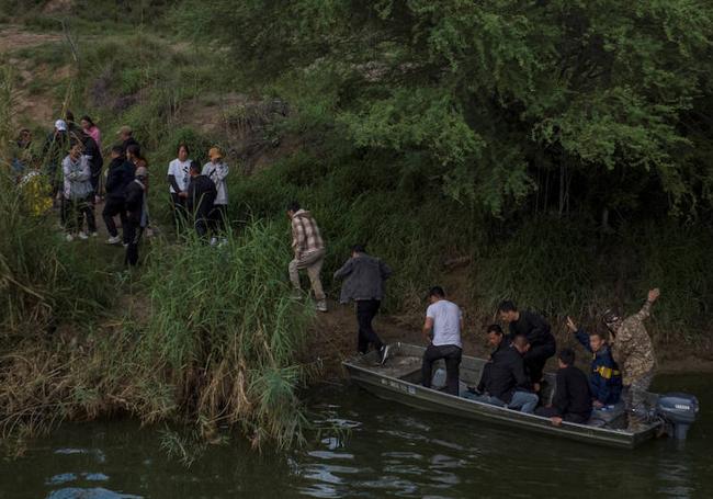 Varios migrantes de China desembarcan de un bote motorizado que han usado para cruzar el Río Bravo hacia los EE UU