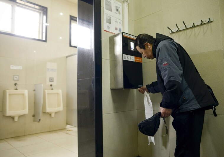 Hombre cogiendo papel en un baño público.