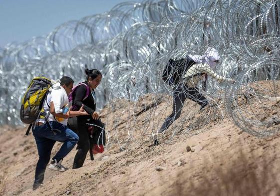 Un grupo de migrantes asciende hacia la frontera a través de los alambres de espino desplegados en la ribera estadounidense del Río Grande.