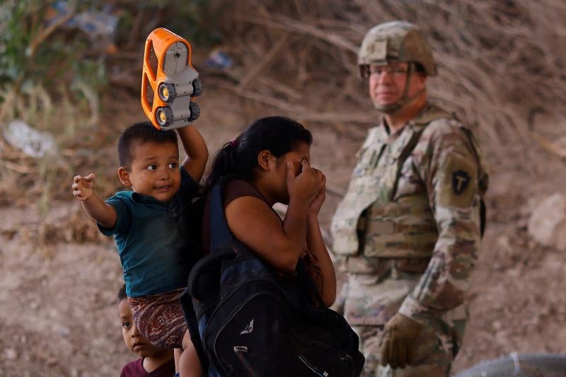 Una mujer camina con dos niños junto a un guardia en Ciudad Juárez.