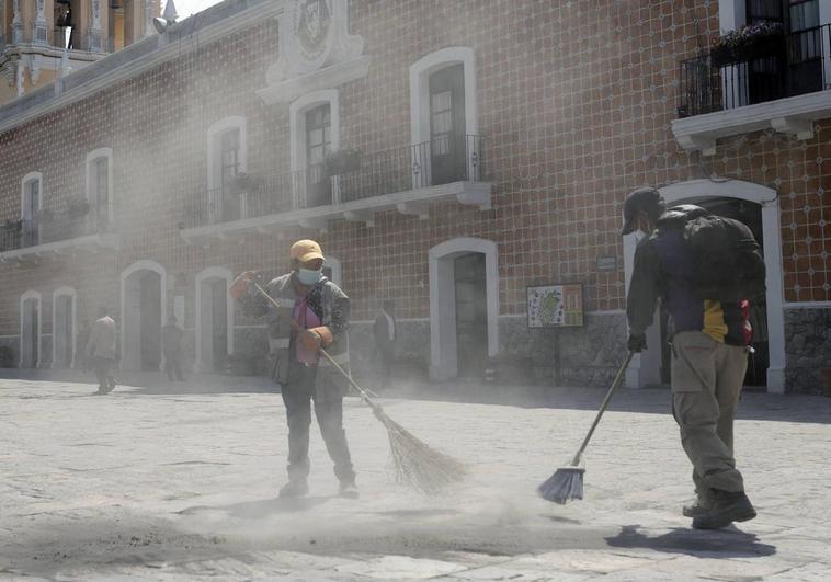 Dos personas barren grandes cantidades de ceniza expulsada por el volcán Popocatépetl en Puebla