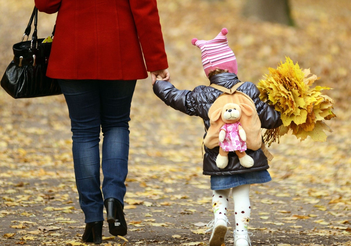 Una madre pasea por un parque con su hija pequeña de la mano.