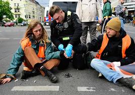 Un oficial de Policía intenta separar las manos de activistas del grupo ecologista 'Última Generación' que se habían pegado al asfalto en señal de protesta en Berlín