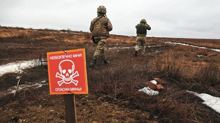 Dos militares caminan por un sendero seguro abierto en un campo minado.
