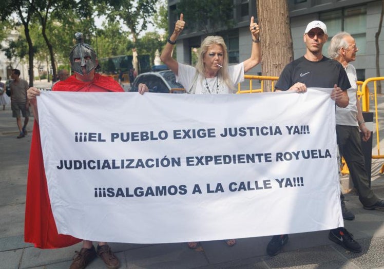 Tres personas con una pancarta en la que se lee, 'El pueblo exige justicia ya!, judicialización expediente Royuela, salgamos a la calle ya', presentes este miércoles en los aledaños de la Audiencia Nacional.