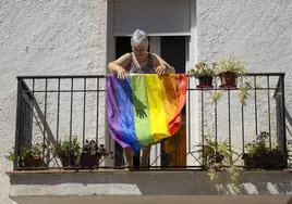 Una vecina de un pueblo valenciano despliega una bandera arcoiris en el balcón de su casa.
