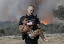 Un policía griego ayuda a evacuar a un niño de un incendio forestal cerca de Atenas