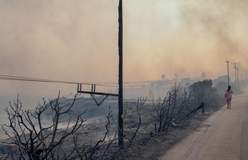 Yangından sonra harap olmuş bir kadın Lindos yakınlarında dumanların arasından yürüyor.