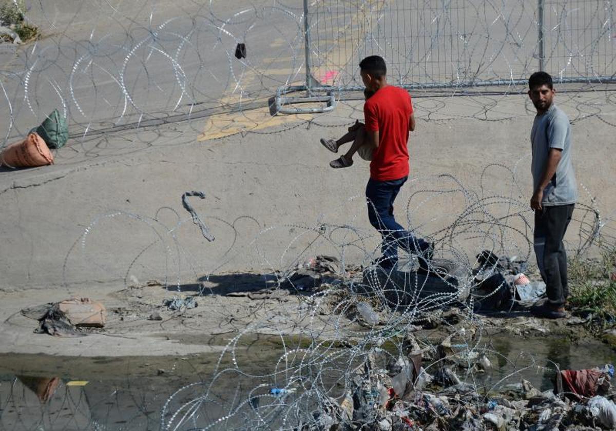 Migrantes cruzan las alambradas colocadas en el muro fronterizo para entregarse a las autoridades estadounidenses y pedir asilo.