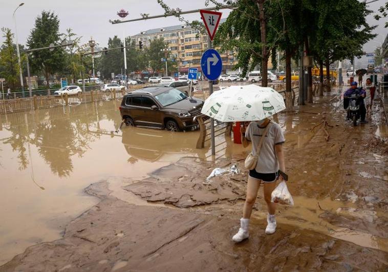 Una mujer camina por una calle cubierta de agua y lodo en el distrito de Mentougou, en Pekín.