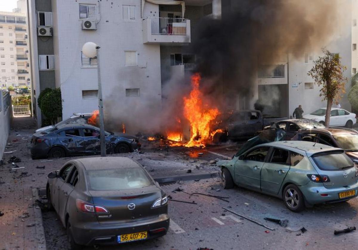 Un miembro de las fuerzas de seguridad israelíes inspecciona una zona bombardeada en Ashkelon, donde varios automóviles arden.