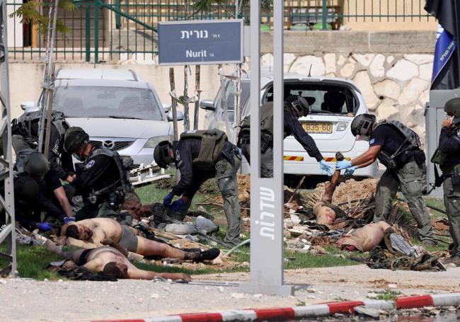 A group of police officers examine the bodies of several Palestinian fighters in front of a police station in the Israeli city of Sderot.