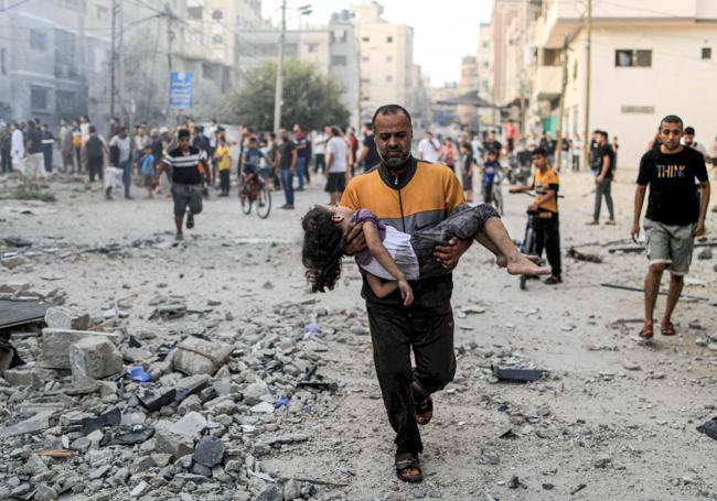 Un gazatí corre con una niña y un bebé tras un bombardeo israelí.