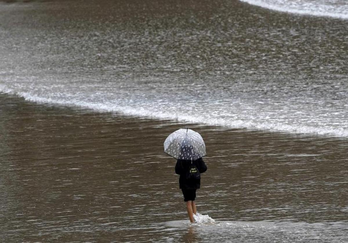 Una mujer con paraguas paseando por la orilla de la playa