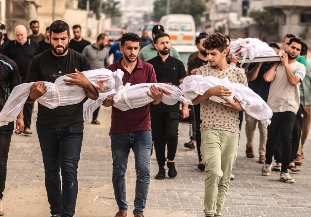 Un grupo de hombres sostiene los cuerpos sin vida de tres pequeños en Gaza.