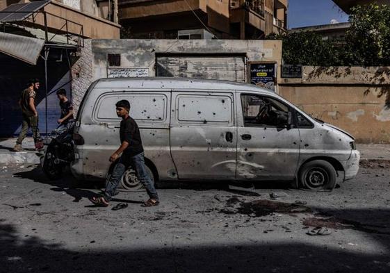 Viandantes caminan junto a un vehículo destruido en la ciudad siria de Idlib.