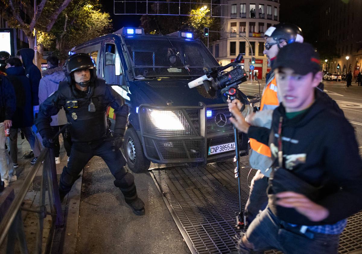 Imagen principal - En la imagen superior, un policía intenta detener a un manifestante; debajo, un grupo de manifestantes con la bandera de España, algunos encapuchados, frente a varios agentes antidistubios; por último, un policía dispuesto a lanzar pelotas de goma tras producirse los primeros altercados violentos. 