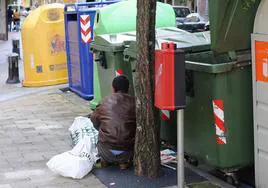 Un hombre busca comida entre los contenedores de basura.