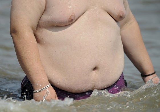 Un hombre obeso se baña en una playa española.