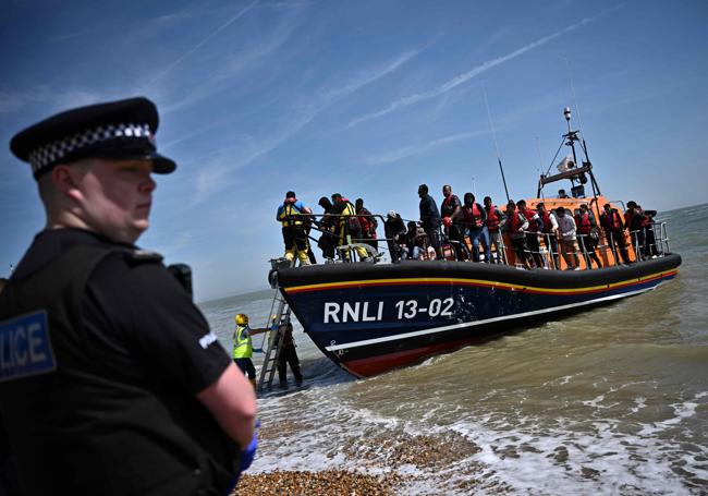 Un oficial británico hace guardia mientras migrantes que intentaban cruzar el Canal de la Mancha desembarcan en la playa de Dungeness.