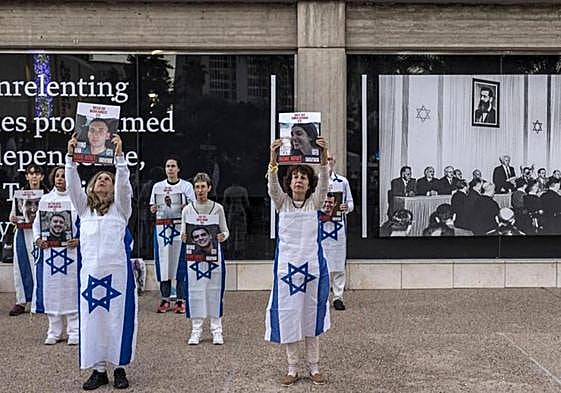 Varias personas envueltas en banderas israelíes sostienen retratos de algunos de los rehene.